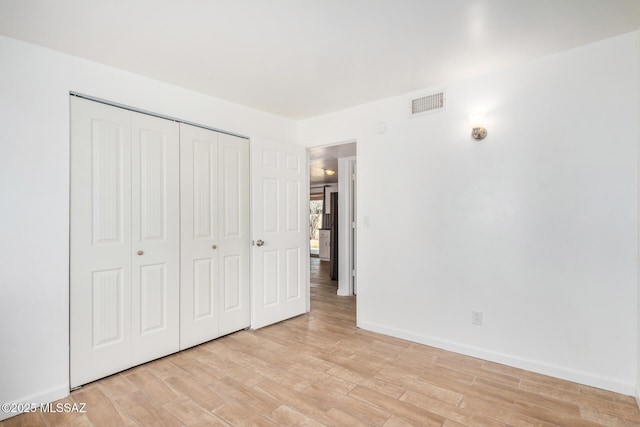 unfurnished bedroom featuring visible vents, light wood finished floors, baseboards, and a closet