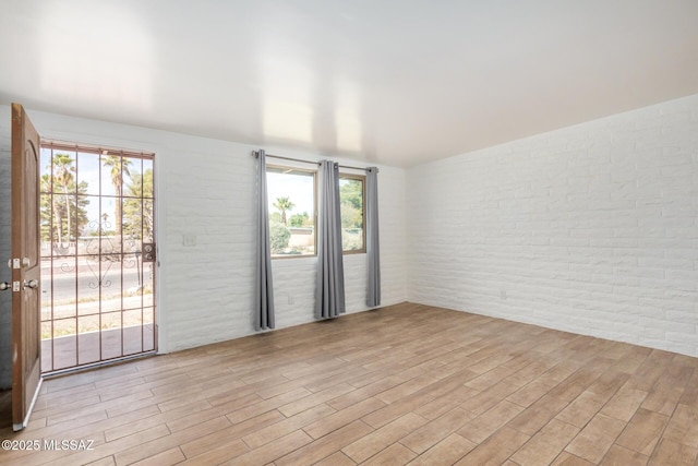 empty room with light wood finished floors and brick wall