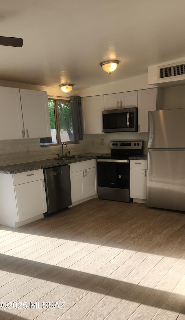 kitchen with light wood-style flooring, stainless steel appliances, white cabinetry, backsplash, and visible vents