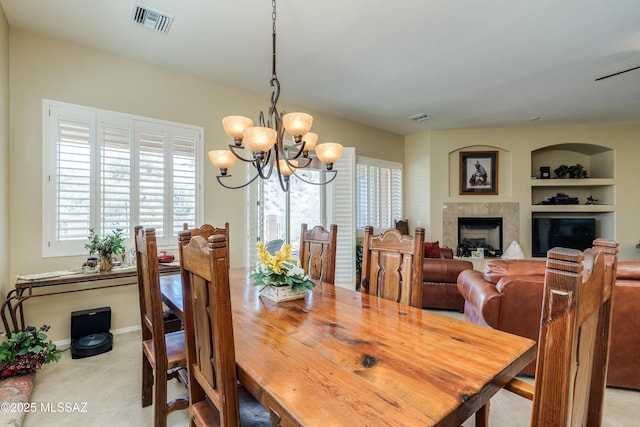 dining space with an inviting chandelier, visible vents, a glass covered fireplace, and built in shelves