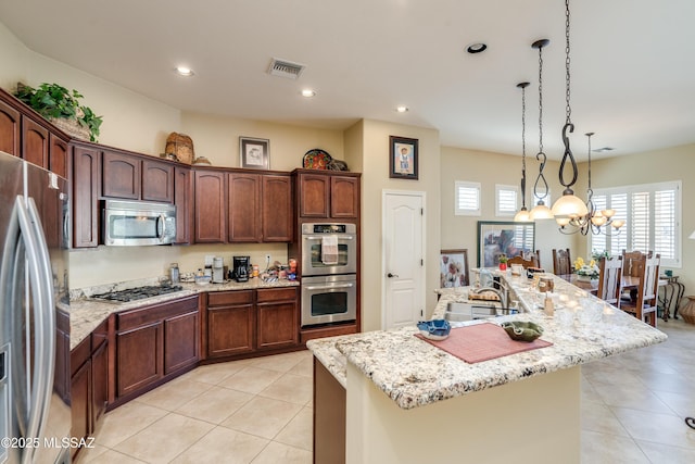 kitchen featuring an island with sink, a sink, stainless steel appliances, light tile patterned floors, and visible vents