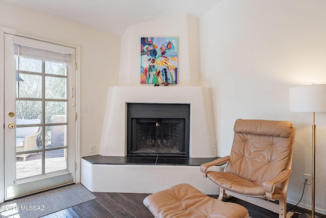 sitting room featuring a fireplace with raised hearth, dark wood-style flooring, and lofted ceiling