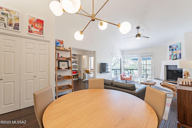 dining area featuring ceiling fan, high vaulted ceiling, a fireplace with raised hearth, and dark wood-type flooring