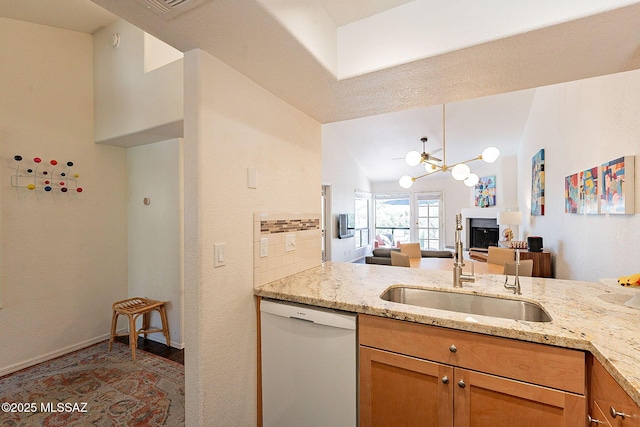 kitchen featuring light stone counters, a sink, vaulted ceiling, dishwasher, and a glass covered fireplace