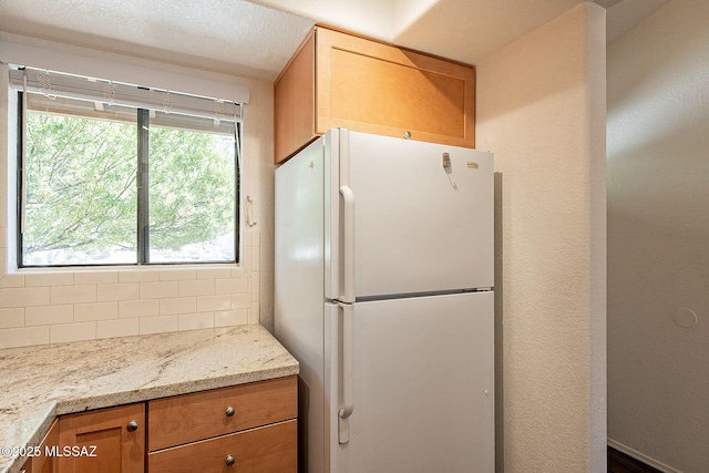 kitchen featuring tasteful backsplash, freestanding refrigerator, a textured wall, and light stone counters