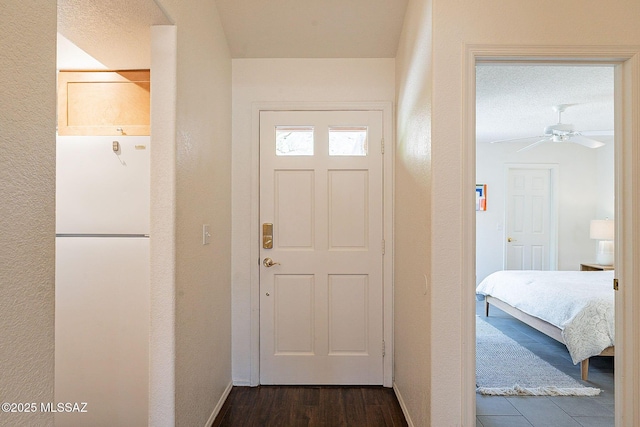 entryway featuring dark wood-style floors, a textured wall, baseboards, and a ceiling fan