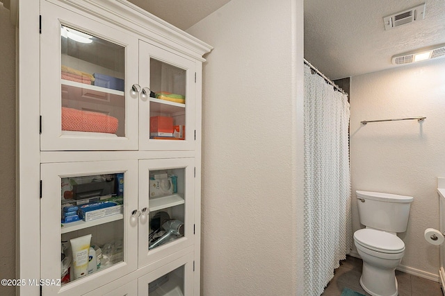 bathroom featuring toilet, tile patterned flooring, visible vents, and a textured ceiling