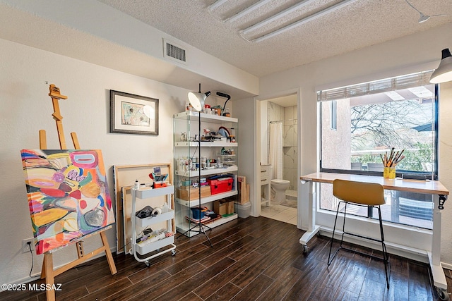 home office with a textured ceiling, visible vents, and wood finished floors