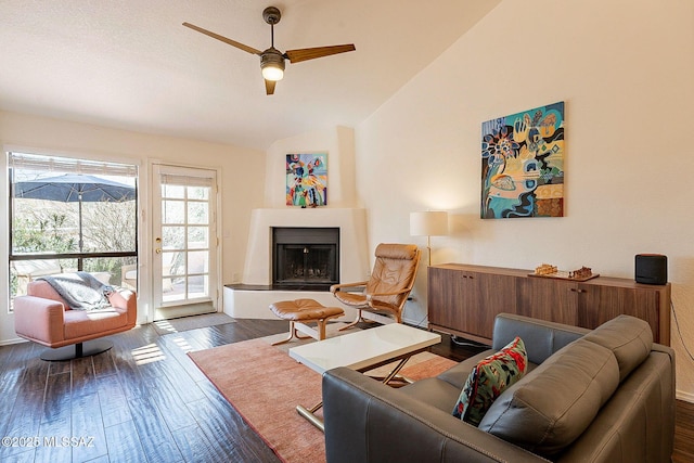 living area featuring dark wood-type flooring, a fireplace with raised hearth, vaulted ceiling, and a ceiling fan