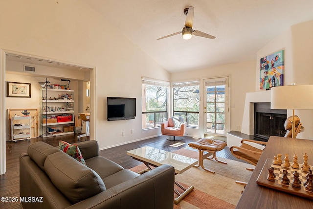 living room with a fireplace with raised hearth, high vaulted ceiling, dark wood-type flooring, visible vents, and a ceiling fan