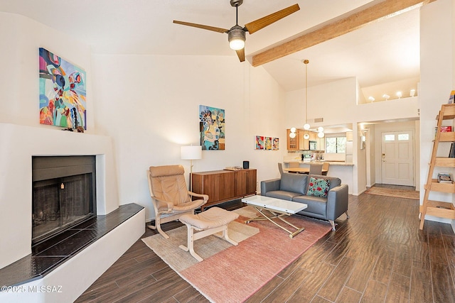 living room with a fireplace with raised hearth, a ceiling fan, beamed ceiling, wood finish floors, and high vaulted ceiling