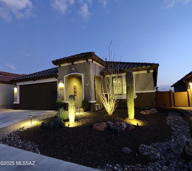 mediterranean / spanish-style home with an attached garage, fence, concrete driveway, a tiled roof, and stucco siding