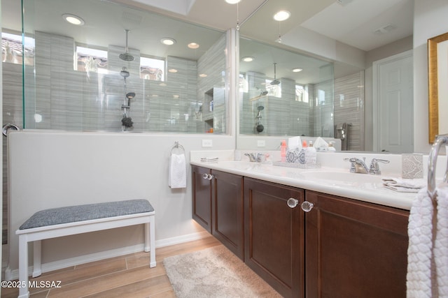 bathroom with double vanity, tiled shower, a sink, and wood finished floors