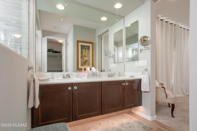 full bathroom featuring double vanity, visible vents, wood finished floors, a spacious closet, and a sink