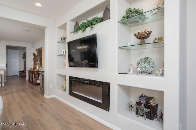 living room with built in features, visible vents, a glass covered fireplace, wood finished floors, and baseboards