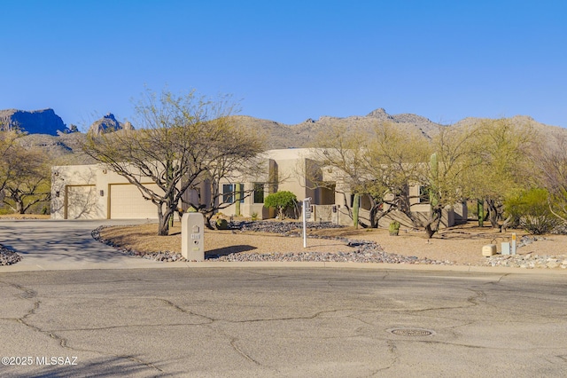 adobe home featuring driveway, an attached garage, a mountain view, and stucco siding