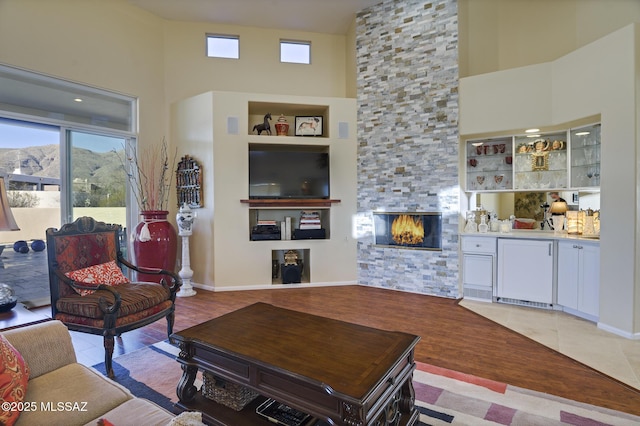 living room featuring a stone fireplace, light tile patterned flooring, built in shelves, and a healthy amount of sunlight