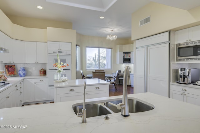 kitchen with built in appliances, backsplash, visible vents, and white cabinets