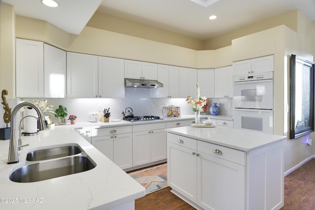 kitchen with white cabinets, white double oven, under cabinet range hood, stainless steel gas stovetop, and a sink