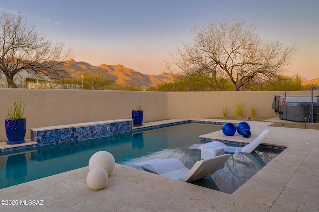 pool at dusk featuring a hot tub, a mountain view, and a fenced in pool