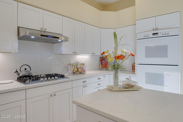 kitchen with white double oven, white cabinets, stainless steel gas stovetop, and under cabinet range hood