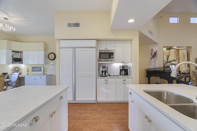 kitchen featuring built in appliances, a sink, visible vents, white cabinets, and light wood finished floors