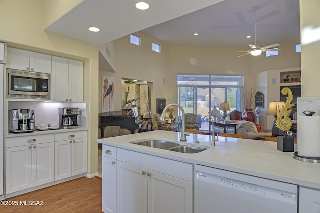 kitchen with white dishwasher, a sink, white cabinetry, open floor plan, and stainless steel microwave