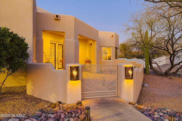 doorway to property with a gate, fence, and stucco siding