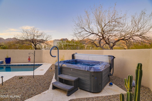 pool at dusk featuring a fenced in pool, a patio, a hot tub, and fence