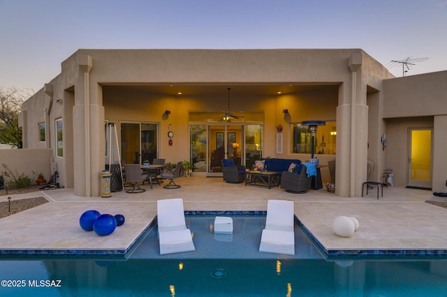 back of house at dusk featuring stucco siding, outdoor lounge area, a patio area, ceiling fan, and an outdoor pool