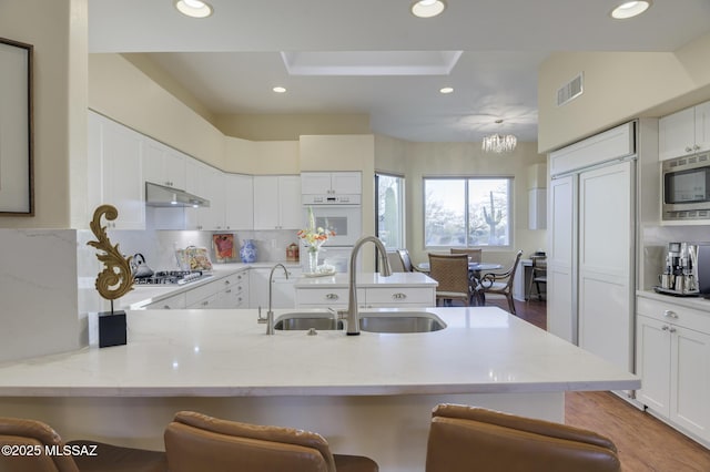 kitchen with built in appliances, under cabinet range hood, a peninsula, a sink, and visible vents