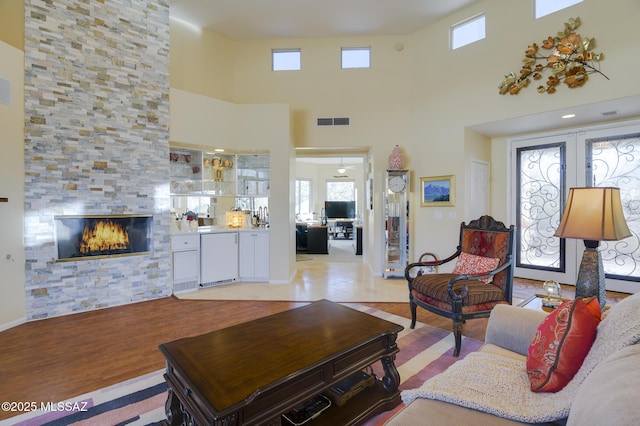 living room with light wood finished floors, a high ceiling, visible vents, and a tile fireplace