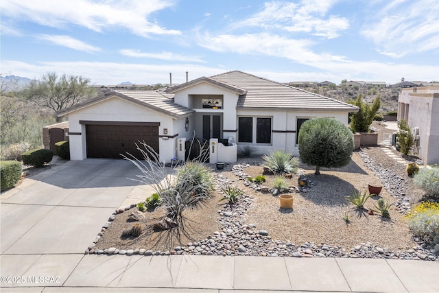 view of front of home featuring concrete driveway, a tiled roof, an attached garage, and stucco siding