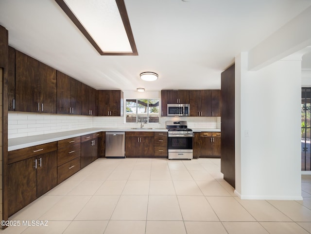 kitchen featuring a sink, light countertops, appliances with stainless steel finishes, dark brown cabinets, and backsplash