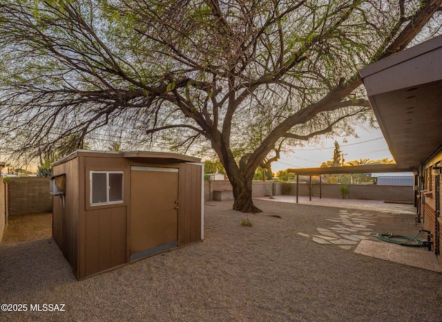 outdoor structure at dusk with a fenced backyard, a storage unit, and an outbuilding