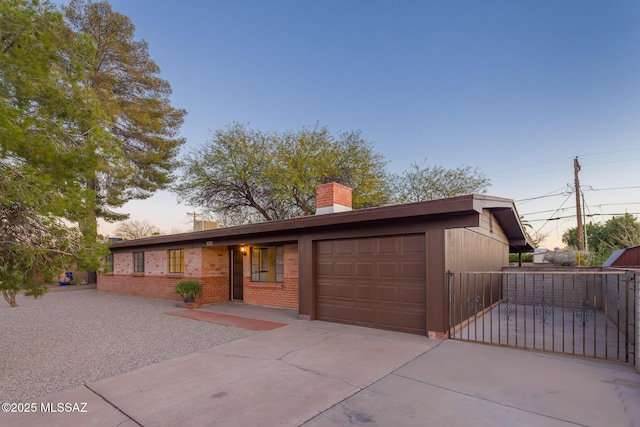 view of front facade with an attached garage, a chimney, concrete driveway, and brick siding