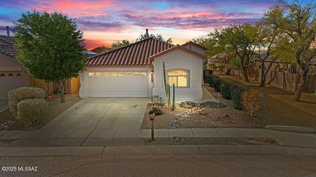 mediterranean / spanish house with a garage, a tiled roof, concrete driveway, and stucco siding