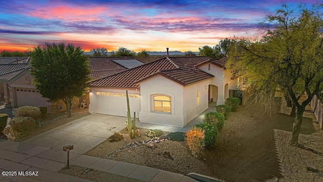 view of front of house featuring a garage, concrete driveway, a tiled roof, roof mounted solar panels, and stucco siding