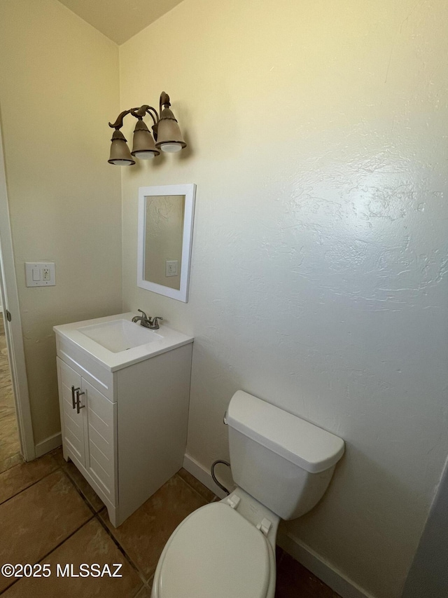 half bathroom with toilet, tile patterned floors, baseboards, and vanity