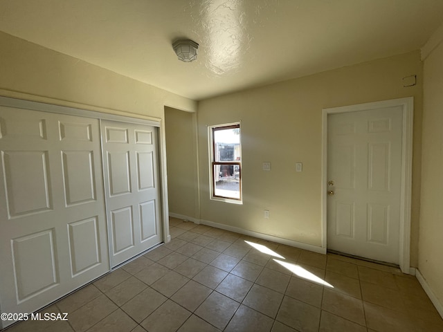 unfurnished bedroom featuring a closet, baseboards, and light tile patterned floors