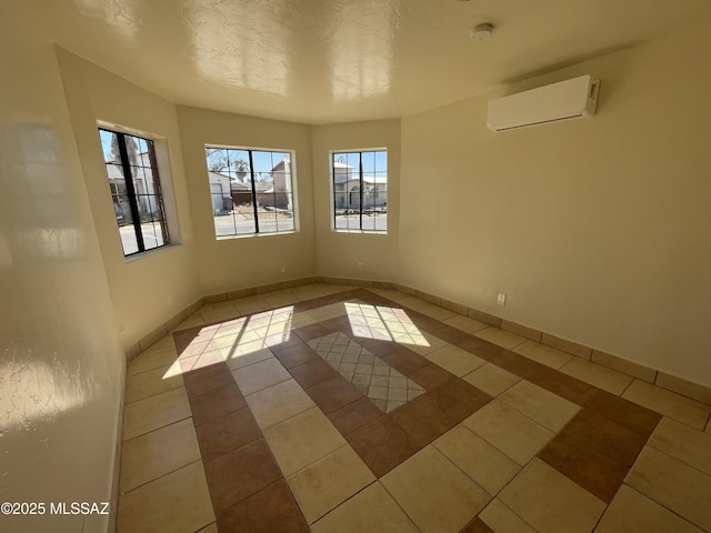 unfurnished room featuring a textured ceiling, a wall unit AC, light tile patterned flooring, and baseboards