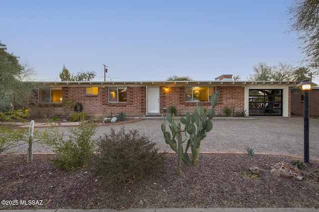 ranch-style home with a garage, gravel driveway, and brick siding