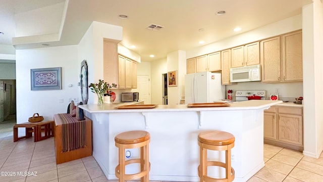 kitchen with a peninsula, white appliances, visible vents, and a breakfast bar area