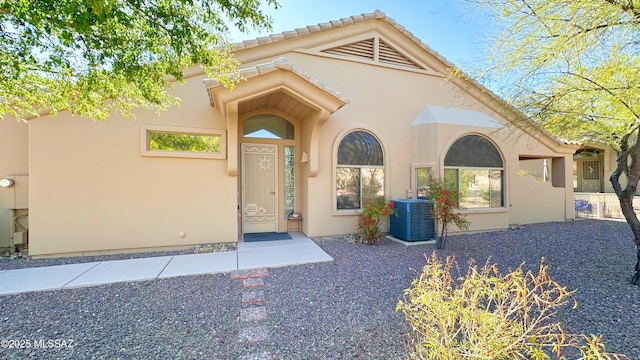 entrance to property with a tiled roof, central AC unit, and stucco siding