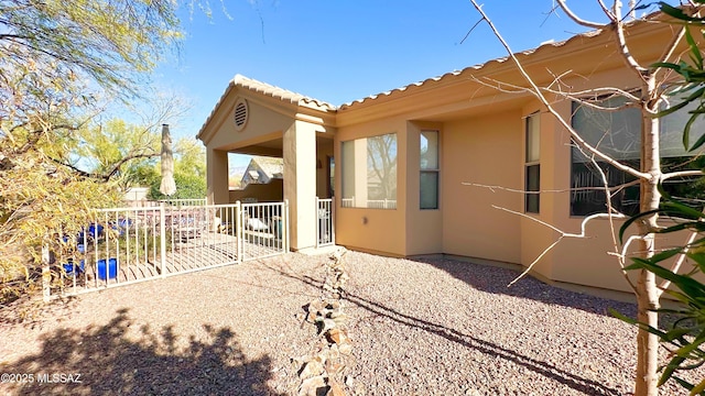 view of side of property featuring a patio area, fence, a tiled roof, and stucco siding