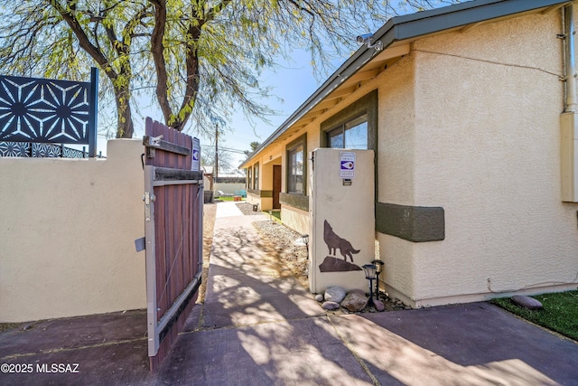 view of side of property featuring fence, a gate, and stucco siding