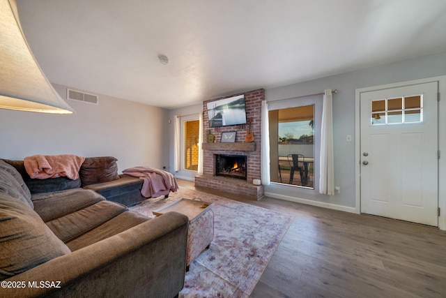 living area featuring a fireplace, wood finished floors, visible vents, and baseboards