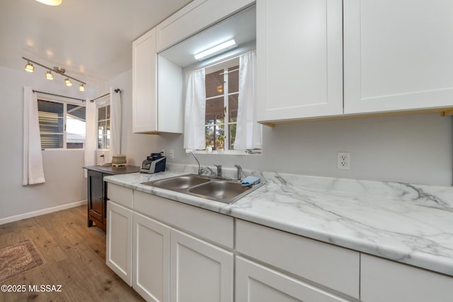 kitchen featuring baseboards, light stone counters, light wood-style floors, white cabinetry, and a sink