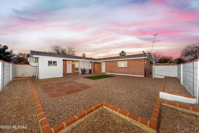 5720 E 4th St, Tucson, AZ 85711 - back of property at dusk featuring a fenced backyard, a patio area, brick siding, and a chimney