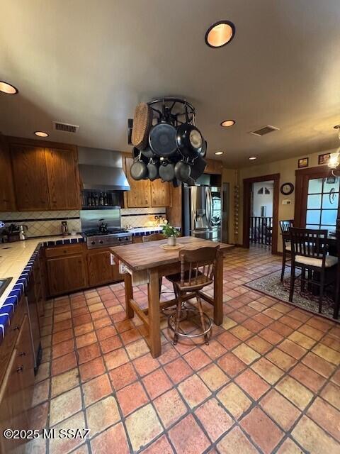 kitchen with stainless steel fridge, visible vents, tile counters, wall chimney range hood, and backsplash